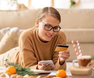 Young casual woman with smartphone and credit card looking at pe