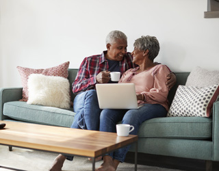 Senior Couple Sitting On Sofa At Home Using Laptop To Shop Onlin