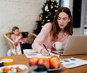Young woman works at home while her daughter stays home on winter vacation