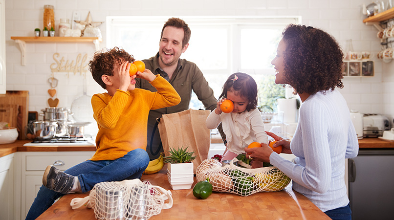 Family Returning Home From Shopping Trip Using Plastic Free Bags Unpacking Groceries In Kitchen