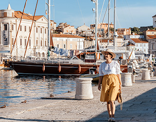 Happy young woman walking in marina with sailing boats in pictur