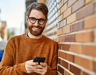 young caucasian man with beard  using smartphone outdoors on a sunny day