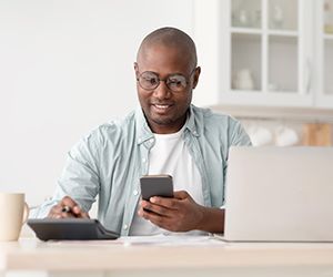 Savings and finances concept. Mature black man using calculator, phone and laptop computer