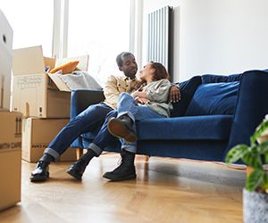 Young Couple In New Home Sitting On Sofa In Lounge On Moving Day