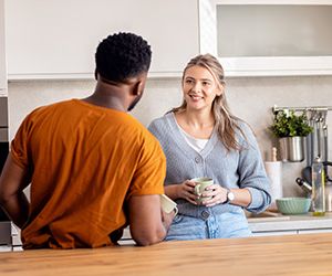 Smiling young mixed couple standing in kitchen drinking coffee a